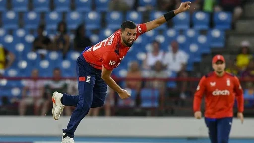 Cricketer bowling during a match in red uniform