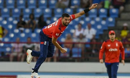 Cricketer bowling during a match in red uniform